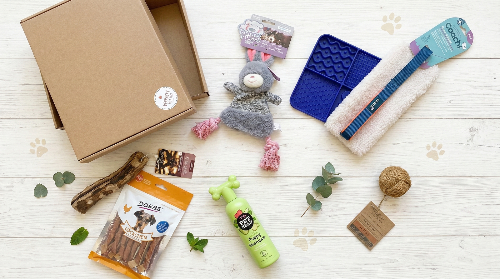Produktübersicht einer PuppyPrep Box auf heller Holzoberfläche mit Spielzeug, Zubehör und Snacks